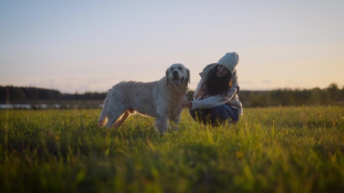 日落时分，一名女子在草地上与金毛猎犬玩耍。抚摸和拥抱狗