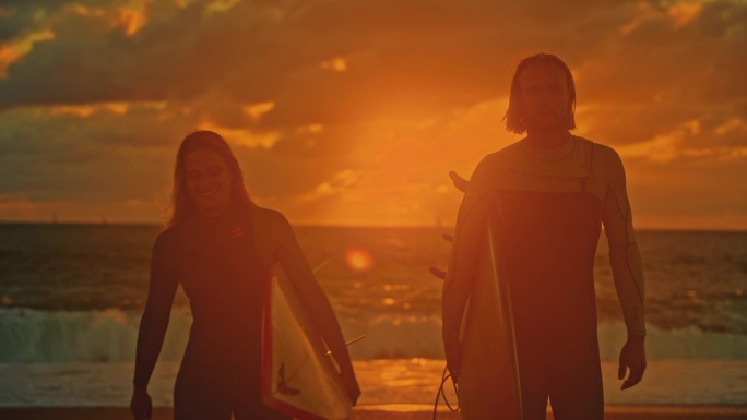 一对冲浪夫妇在日落的海滩上玩冲浪板