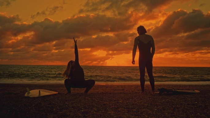夕阳下，一对冲浪夫妇在夏日的海滩上伸展着冲浪板
