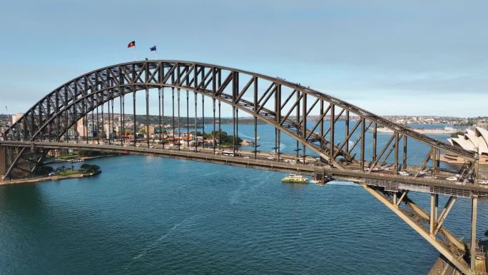 电影航拍镜头平移从悉尼海港大桥，桥下露出悉尼歌剧院，悉尼地标日落，澳大利亚。(Slowmo)