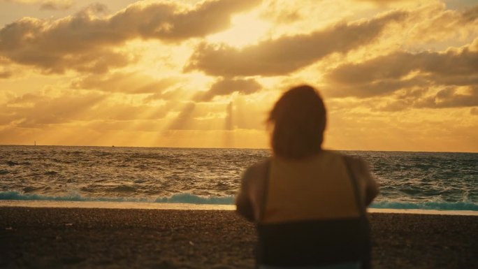 宁静的人看着美丽的日落天空在海洋。宁静的人坐着，看着大海上美丽的日落天空。他起身奔向海浪，