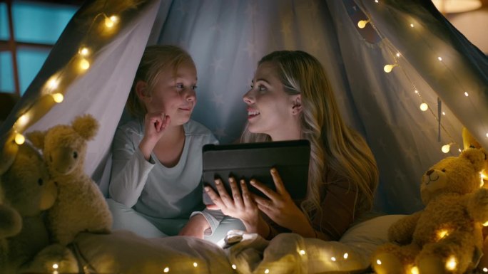 母亲、孩子和平板电脑在黑暗中学习，卧室和灯在舒适中，在家一起照顾。妇女、女儿和纽带在语言习得中的教育