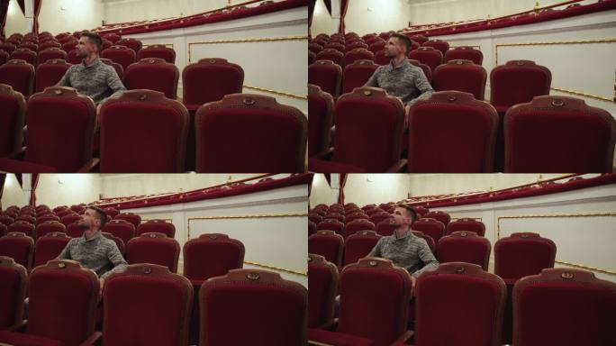 剧院大厅里，身穿套头衫的西班牙裔男子坐在昂贵的天鹅绒扶手椅上。