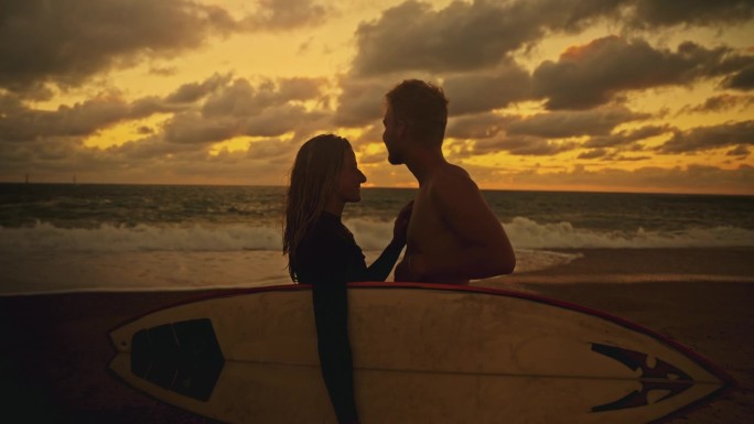 深情的冲浪夫妇拥抱，看着日落的海洋
