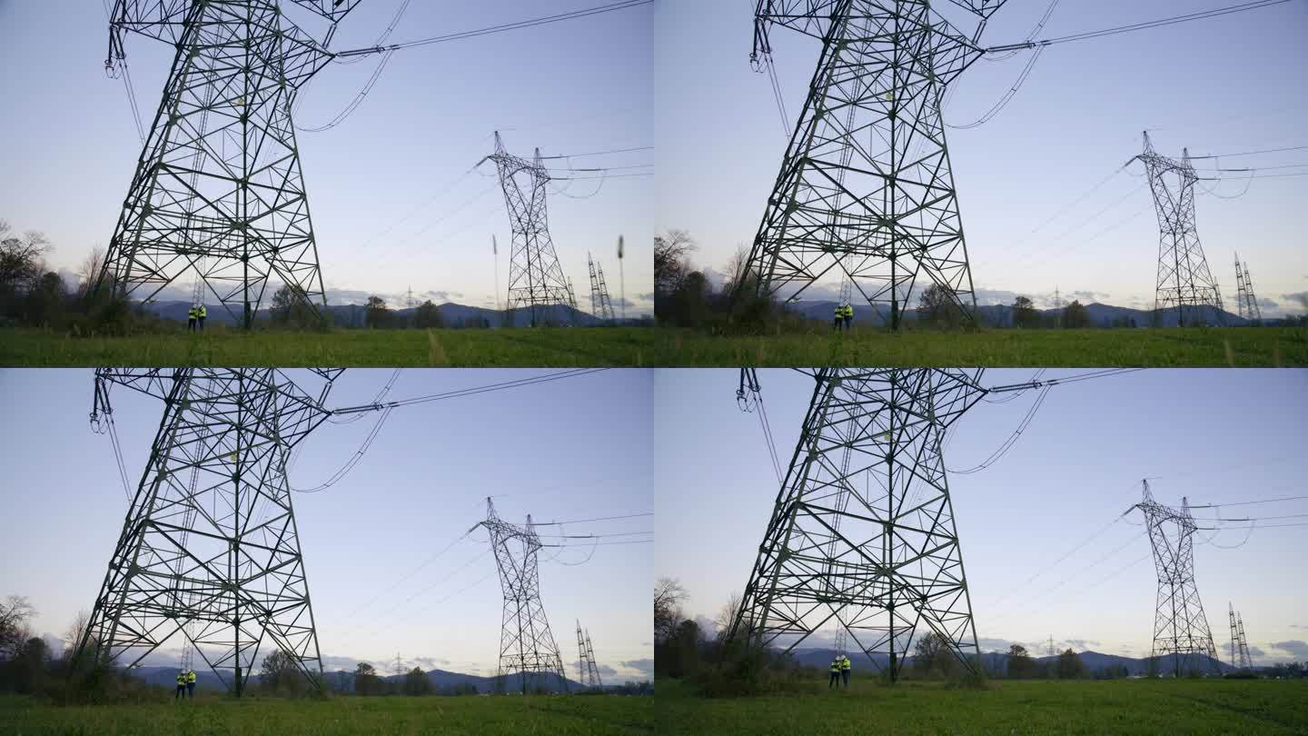 站在电厂草地上的电塔下的电机工程师面对蓝天