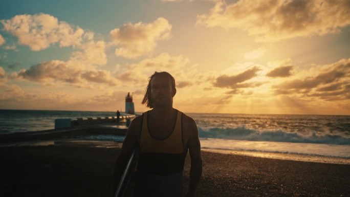 夕阳下，男冲浪者拿着冲浪板在海边慢跑
