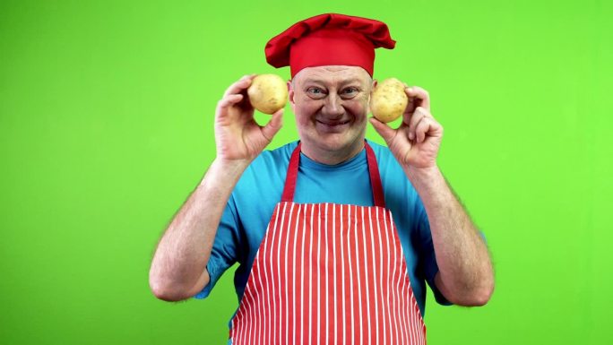 快乐微笑的高级厨师用手捂着眼睛，手里拿着两个土豆。