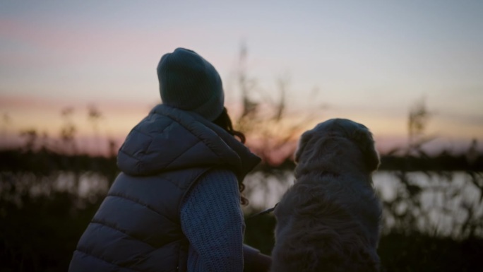 一个女人和她的金毛猎犬坐在草地上一起看日落