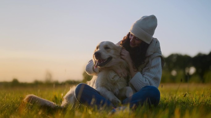一个女人在草地上和一只金毛猎犬玩耍。亲吻和拥抱腿上的狗
