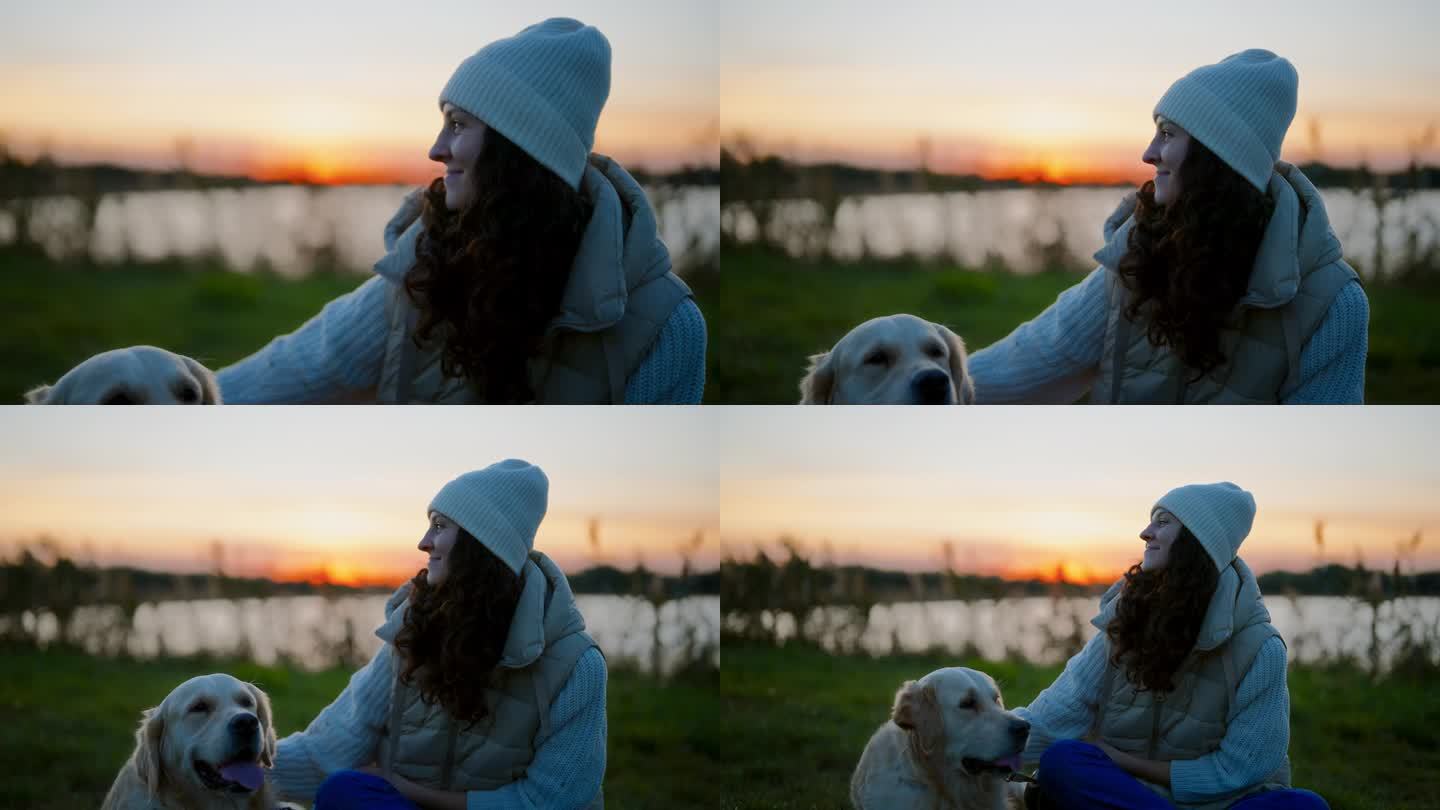日落时分，一名妇女和一只金毛猎犬在湖边的草地上休息。抚摸和拥抱狗