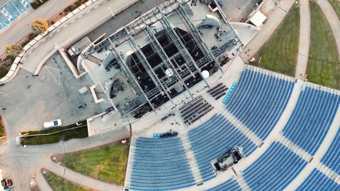 无人机在一个古老的圆形剧场上空旋转拍摄，巨大的舞台上有巨大的屏幕，草地和座位，黄金时间以色列。4K视