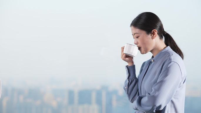职业女性在办公室落地玻璃窗前喝咖啡