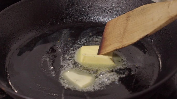 木抹刀搅拌融化黄油在热铸铁锅覆盖底部
