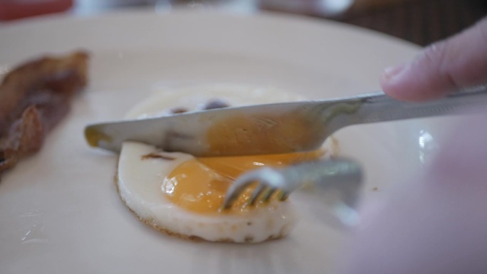 用刀叉切蛋黄吃白盘子里的煎蛋。切单面鸡蛋，蛋黄溏心