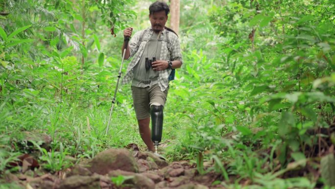 中年成年亚洲男性，装上假肢，在观鸟观光后走下山顶，开朗的残障男子喜欢在森林里徒步，放松身心