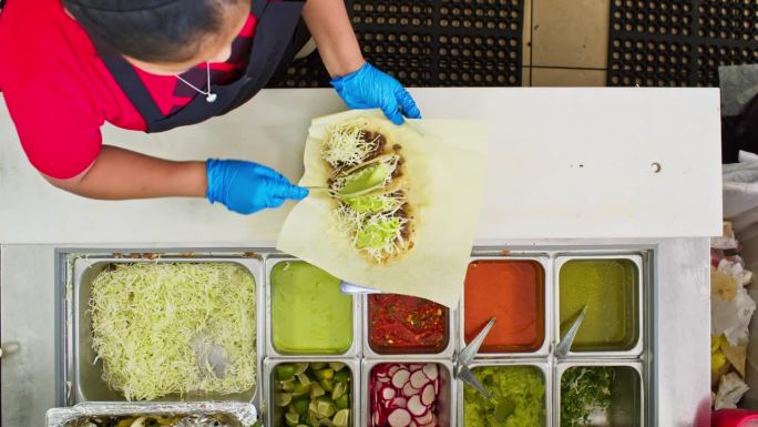 餐厅工作人员在墨西哥餐厅往玉米饼里加配料的俯视图
