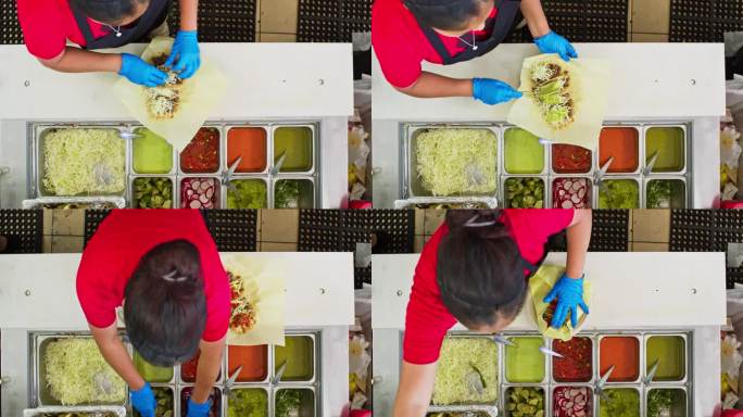 餐厅工作人员在墨西哥餐厅往玉米饼里加配料的俯视图