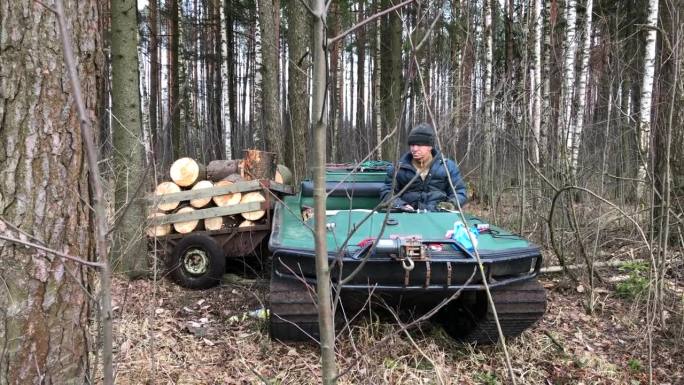 森林里的老人，坐在一辆全地形车上，抽着烟，正准备把砍下来的锯树放在手推车上送到锯木厂去。