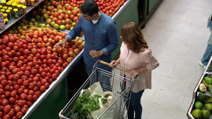 一对拉丁美洲夫妇在市场上一起推着购物车购买新鲜农产品，一边聊天一边添加产品