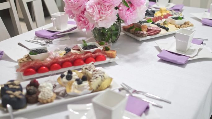 一张摆着茶点和早餐的糖果桌的特写镜头。粉红色的花在中间。紫色的餐巾在盘子下面