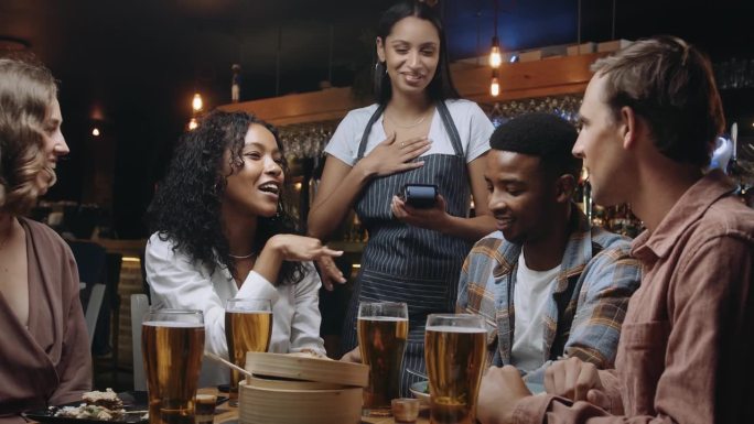 女服务员在餐厅给一群朋友送卡片机。其中一名妇女通过在卡片机上敲手机来支付晚餐的费用。