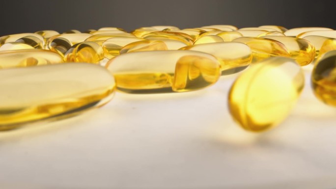 透明胶囊，白色背景上含有维生素和脂肪酸。药品生产。鱼油黄金胶囊，支持健康。ω- 3