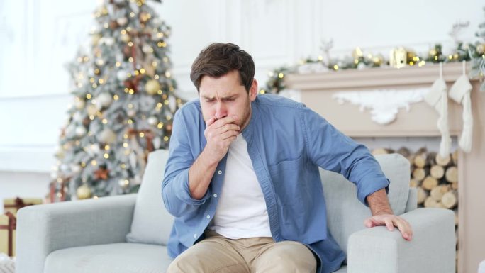 一名男子在冬季、新年、圣诞节、圣诞节期间，坐在家里客厅的沙发上，恶心得想吐