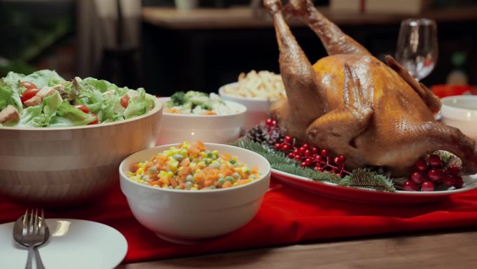 在家庭生活家庭的圣诞庆祝活动中，餐桌上摆放着烤鸡、什锦蔬菜沙拉、炸土豆、汤、披萨等各种食物，配上一杯