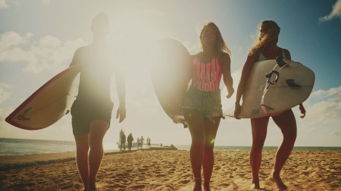 美丽的年轻人穿着泳装，背着冲浪板在海滩上散步。大海与波浪和太阳的背景