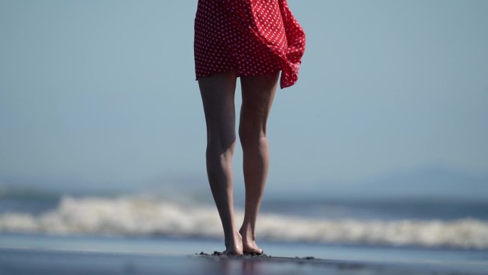 后视图赤脚女人的腿走在潮湿的黑色沙滩上。长而纤细的脚踏女性腿。慢动作，手持拍摄
