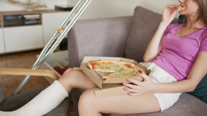 腿上打石膏的女人坐在沙发上吃披萨