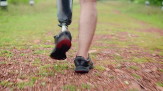 亚洲残障男子假腿行走在森林附近长满草的土路上的特写，中年男性利用闲暇时间在户外散步锻炼，以获得积极情