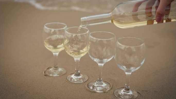 在四个杯子里倒白葡萄酒，排排站在海边的湿沙滩上