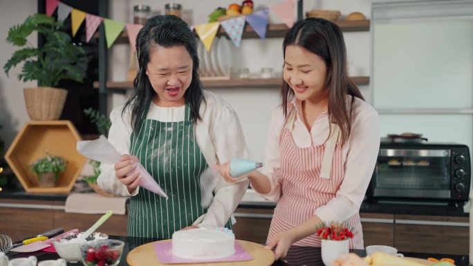 快乐的亚洲老母亲和小女儿一起帮忙把奶油挤到蛋糕上。自制糕点，烹饪蛋糕。家庭与烹饪理念