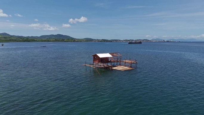 一个木制的渔夫小屋，建在浅水区的高跷上，远处是山地景观。巴里巴荣，苏里高市-菲律宾。白天，无人机拍摄