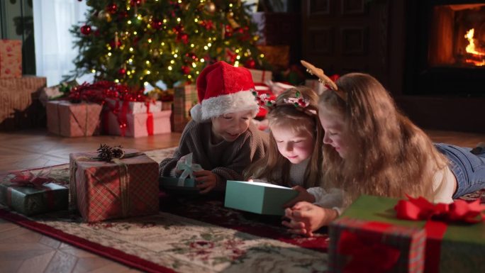 圣诞快乐。孩子们在圣诞树旁打开礼品盒。客厅里有圣诞树壁炉的孩子们带着惊讶的表情打开礼盒。平安夜在家。