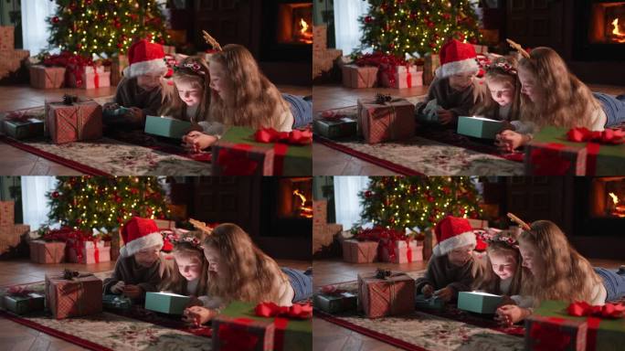 圣诞快乐。孩子们在圣诞树旁打开礼品盒。客厅里有圣诞树壁炉的孩子们带着惊讶的表情打开礼盒。平安夜在家。