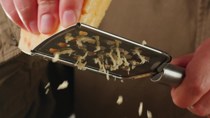 意大利奶酪磨碎器特写，磨碎的奶酪的特写，磨碎的面食或披萨。厨师在咖啡厅烹饪帕尔马干酪或豪达干酪。