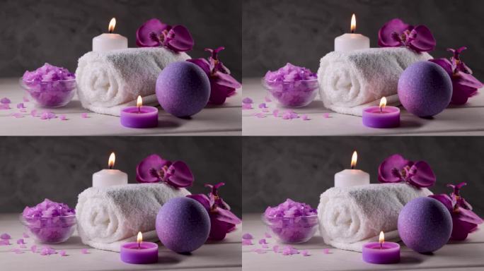 紫色浴弹，海盐晶体，毛巾和燃烧的香薰蜡烛在木桌上。身体皮肤护理。健康水疗中心