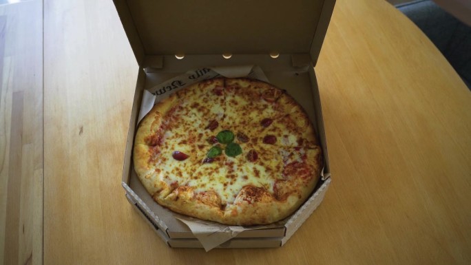 用手打开家里桌子上的纸板箱的意大利披萨的照片