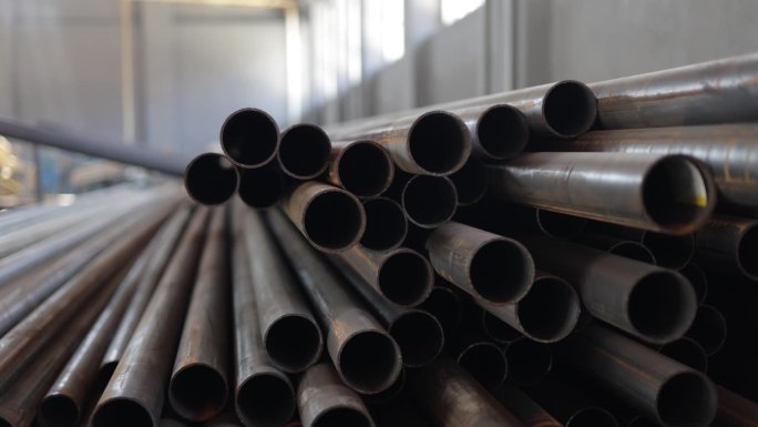 在现代工业工厂宽敞的仓库中，大量的大直径金属管道堆放在一起。圆形建筑材料等待装运。工业概念。
