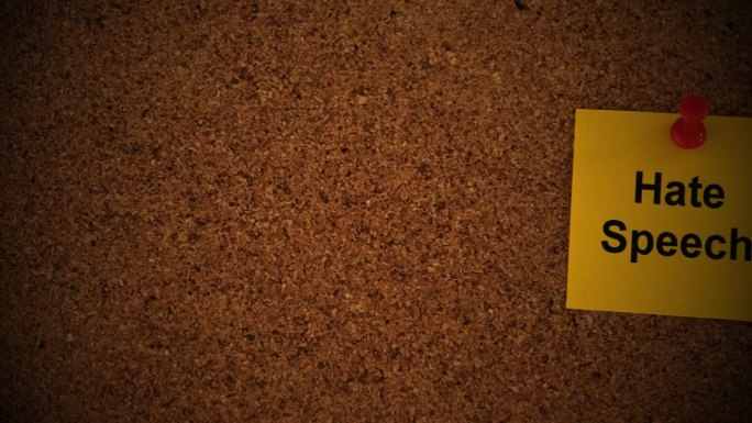 一张黄色的纸条，上面写着“仇恨言论”，别在一块软木板上。