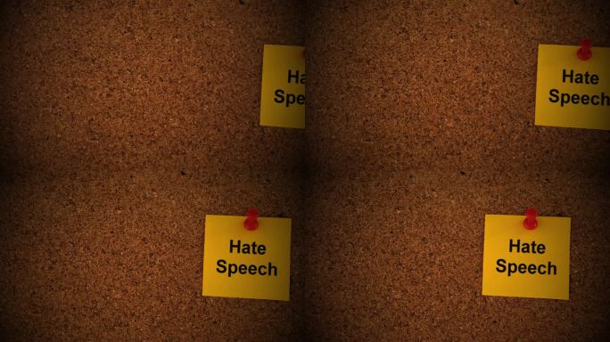 一张黄色的纸条，上面写着“仇恨言论”，别在一块软木板上。