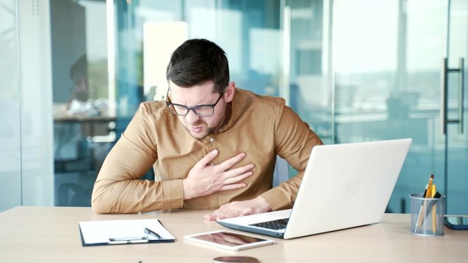 一位年轻的商人在办公室用笔记本电脑工作时突发心脏病