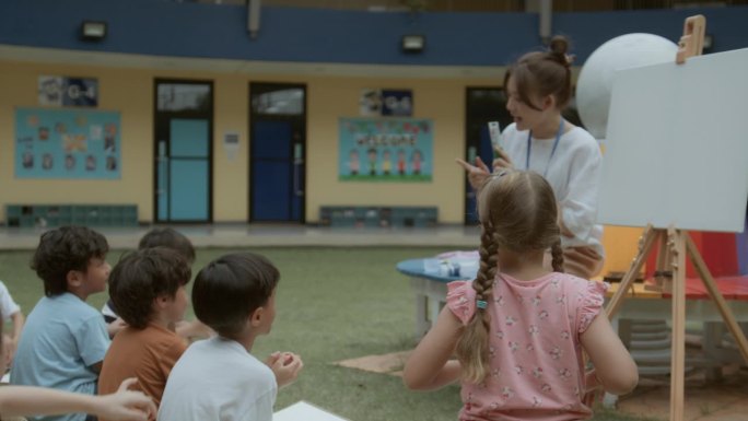 一位兴高采烈的亚洲老师在教室外和小朋友们聊画画。