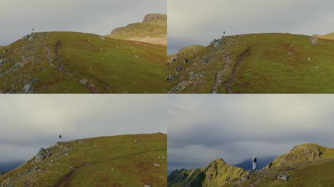 无人机沿着绿色的草地飞向站在峡湾山顶的男性旅行者，面对着挪威大海的壮丽景色