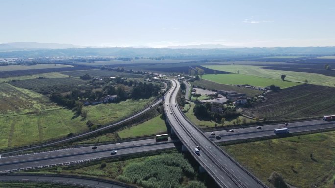 鸟瞰一条沥青高速公路，它穿过生长在乡村的树木，围绕着一条由桥梁连接到当地城镇的道路