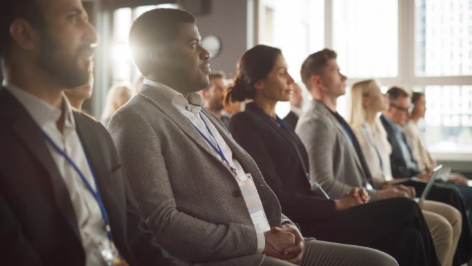 一名非洲男子坐在科技会议拥挤的礼堂里。专业商人聆听主题演讲。专家观看新软件解决方案的创新技术展示。