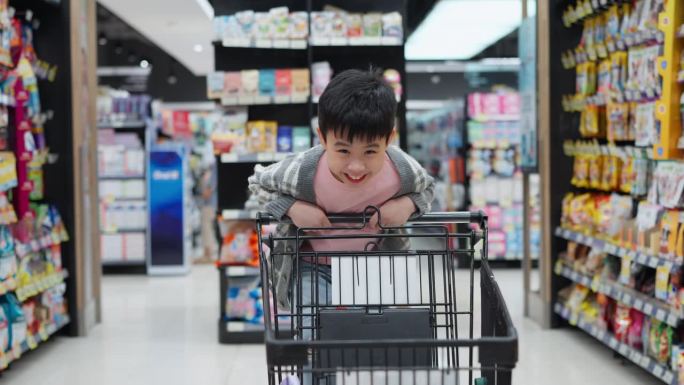 一个小男孩站在购物车上，热情地推着购物车。灿烂的笑容和无忧无虑的姿态，体现了与家人一起购物冒险的纯粹