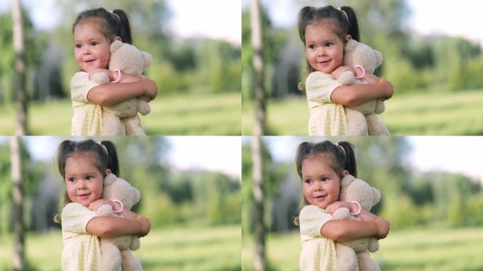 可爱的小女孩在公园里抱着泰迪熊，幸福的家庭宝宝孩子的梦想概念，幼儿园，孩子们在公园的草地上晒太阳的夏